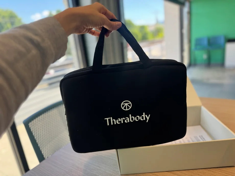 A person holds out a compact carrying case for the Therabody Thermback LED