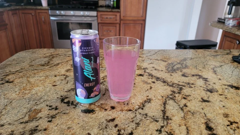 A glass of Alani Nu rests next to the can.