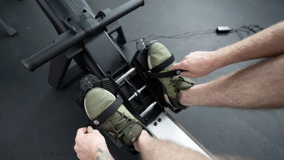 A person straps their feet into the Aviron Strong Series Rower