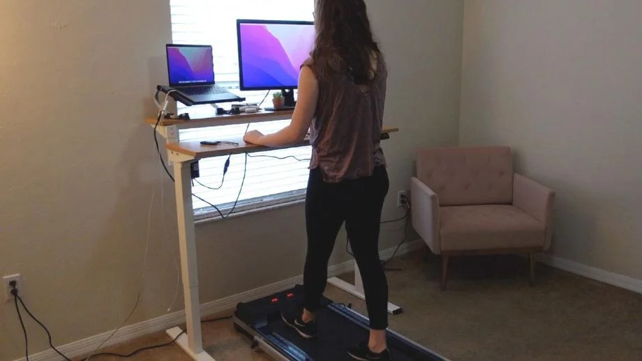 A woman is shown using the Redliro Under Desk Treadmill while working at a standing desk.
