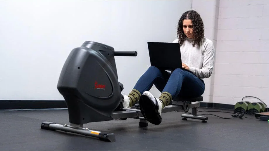 Our tester using a fitness app on a laptop while working out on a rowing machine
