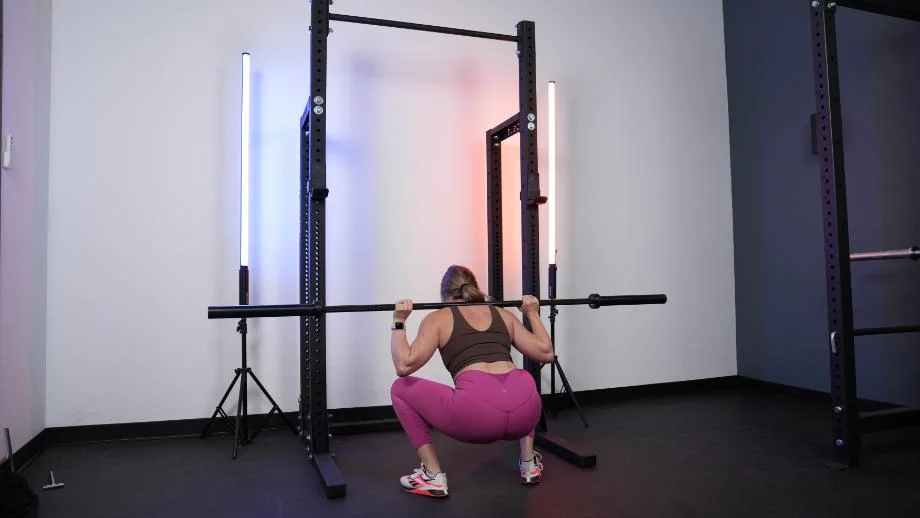 A woman squatting on the Rogue HR-2 Half Rack with blue and orange light bars against the wall on either side of the rack
