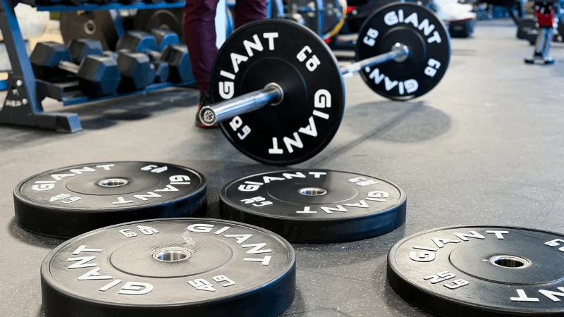 Multiple GIANT Lifting Base Bumper Plates on a gym floor next to a loaded barbell