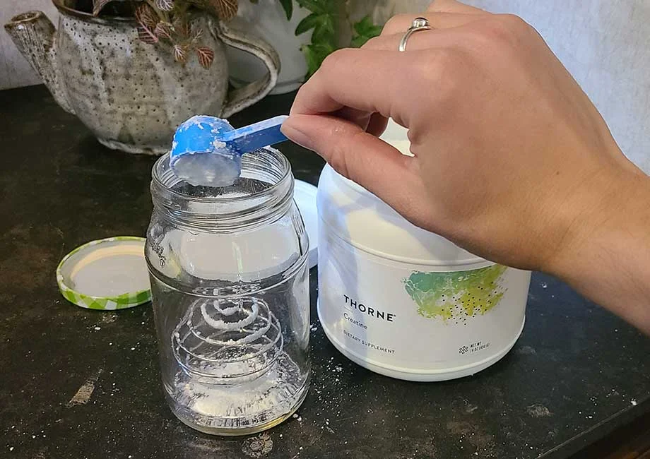 A hand pours a scoop of Thorne Creatine powder into a jar.