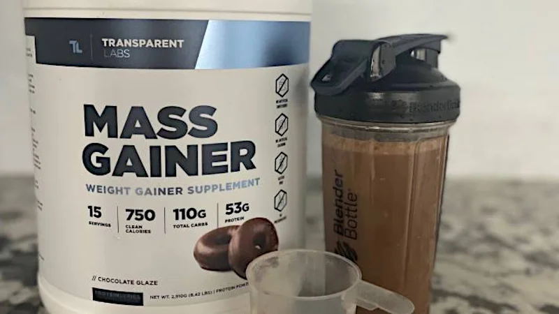 A shaker bottle full of Transparent Labs Mass Gainer next to the container.