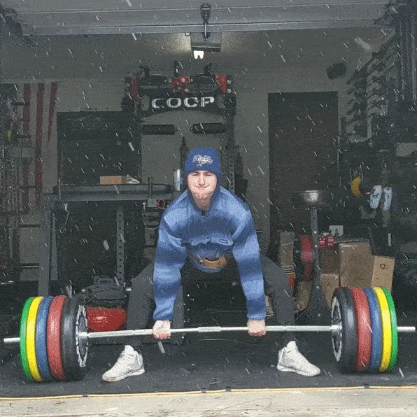 man deadlifting heavy barbell in garage gym during snow storm