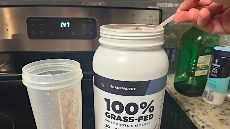 A hand scooping from a container of Transparent Labs Whey Isolate Protein.