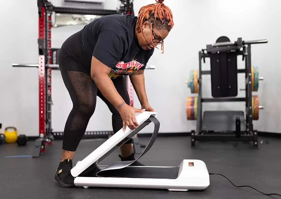 Woman in leggings and a t-shirt folding up the WalkingPad