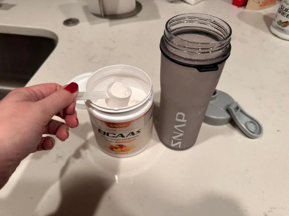 A person taking out a scoop of Snap Supplements BCAA Powder from the container