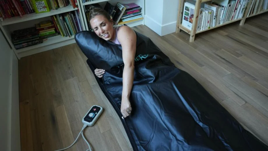 A woman lying on the floor next to a bookshelf while using a HigherDOSE infrared sauna blanket