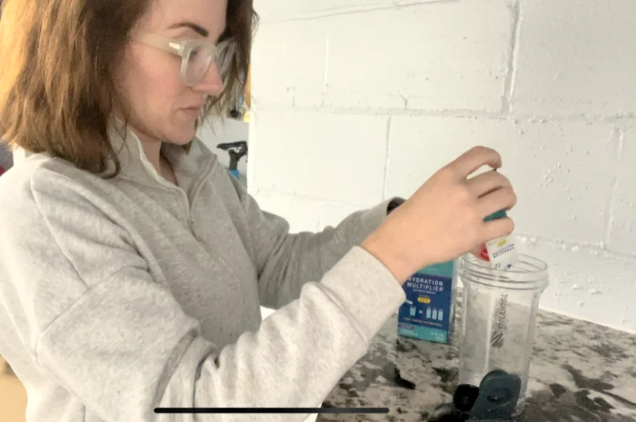 A woman pours Liquid IV Hydration Multiplier into a shaker bottle