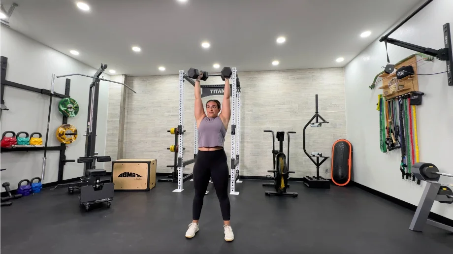 A woman performing the standing dumbbell shoulder press exercise.
