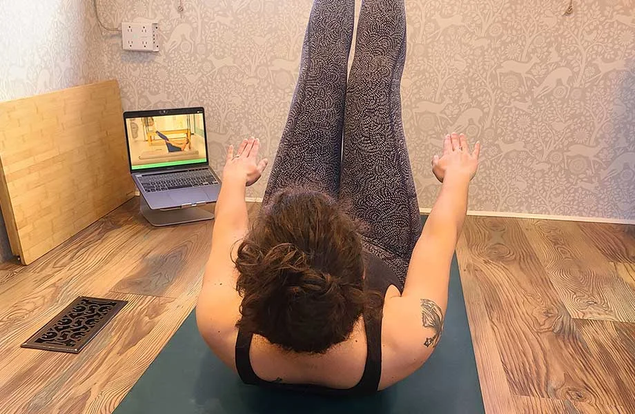 A woman follows a Pilatesology video.