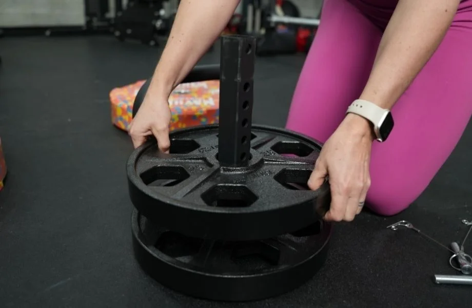 A woman putting a weight plate on the Titan Fitness Plate Loadable Kettlebell Swing