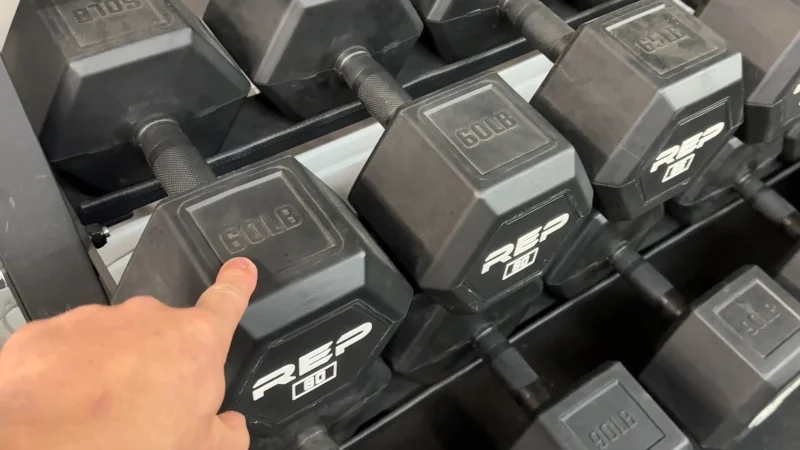 pointing-to-one-rep-fitness-rubber-coated-hex-dumbbell-of-many Pointing out a REP Fitness Rubber Coated Hex Dumbbell on a rack of many.