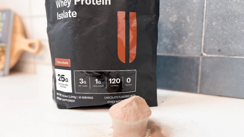 An open container of NOBULL Grass-Fed Whey Protein Isolate next to a full, rounded scoop of powder