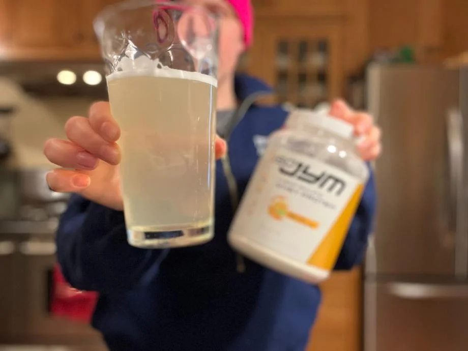 A person holds out the container and a shake of ISO JYM 100% Whey Protein.