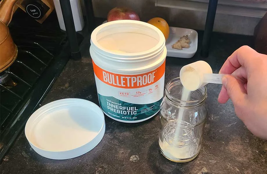 Pouring a scoop of Bulletproof InnerFuel Prebiotic into a glass jar.