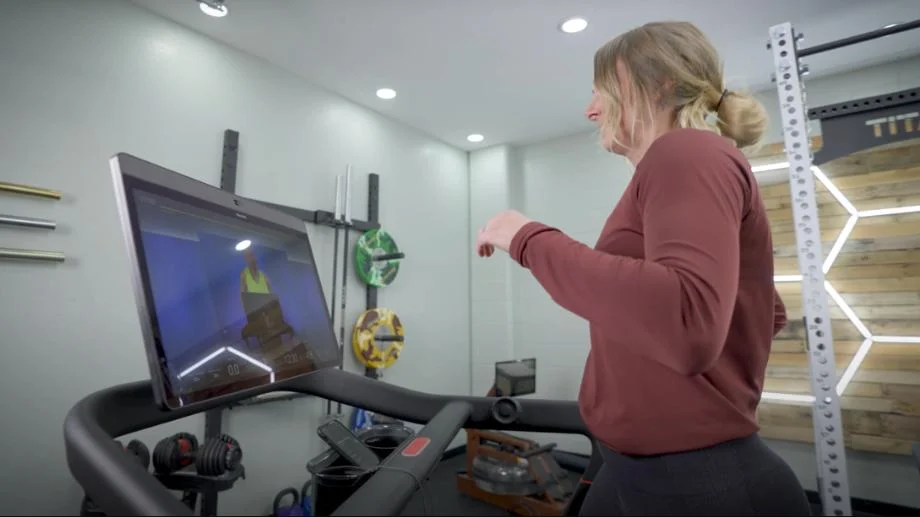 A woman runs on the Peloton Tread while looking at the HD touchscreen