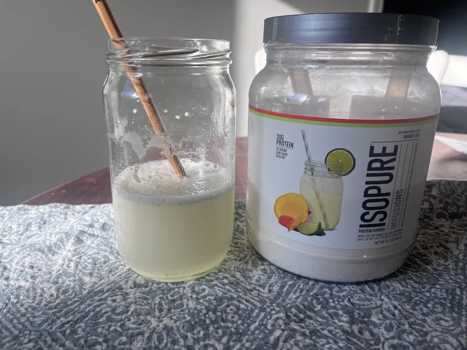 Isopure Clear Whey protein is shown mixed in a glass next to the container.