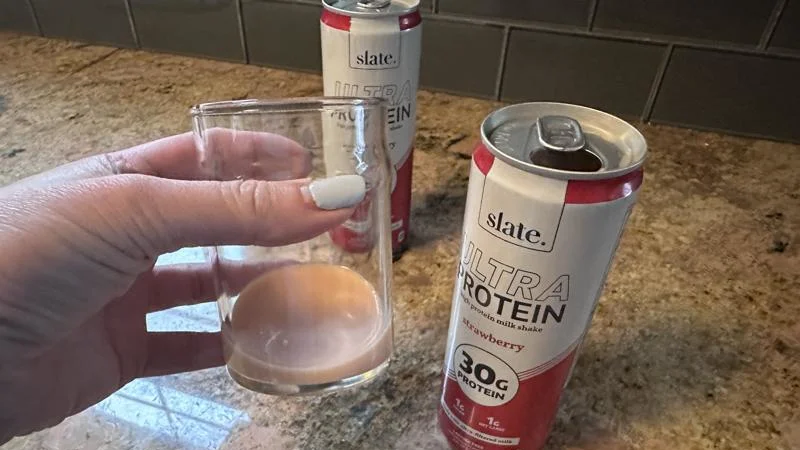 A hand holding up a glass of Slate Protein Powder