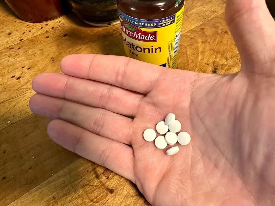 A hand holds some Nature Made Melatonin tablets.