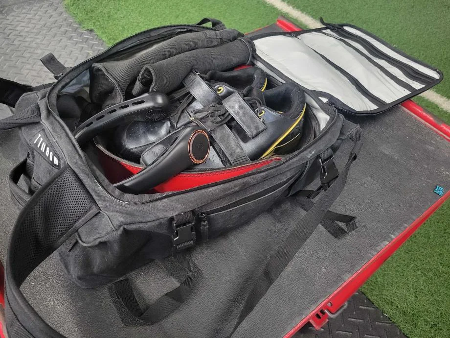 A NOBULL Waxed Canvas Duffleback that's been packed to the brim with gym equipment.