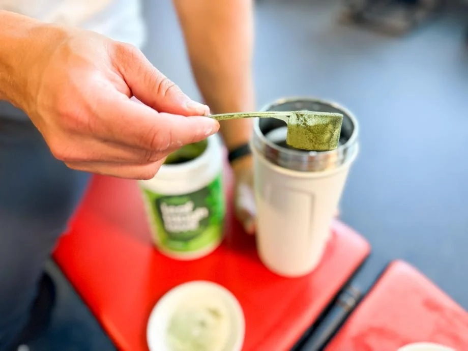 Pouring a scoop of Wellah Leaf, Laugh, Love Supergreens into a shaker cup