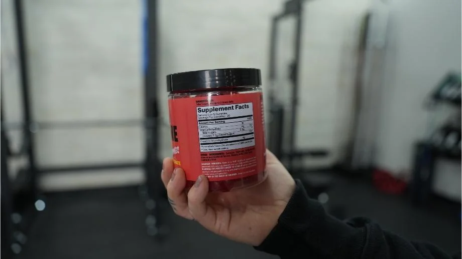 A person holds up the Supplement Facts label on a tub of Swoly Creatine Gummies.