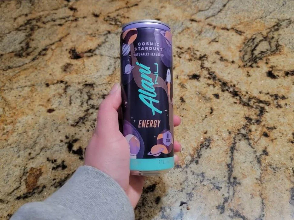 A hand holds out a can of Alani Nu.