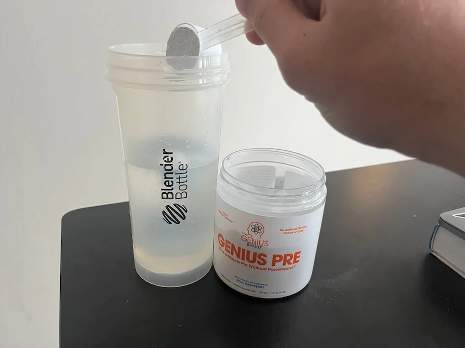 Scooping Genius Pre Workout into a shaker cup with water