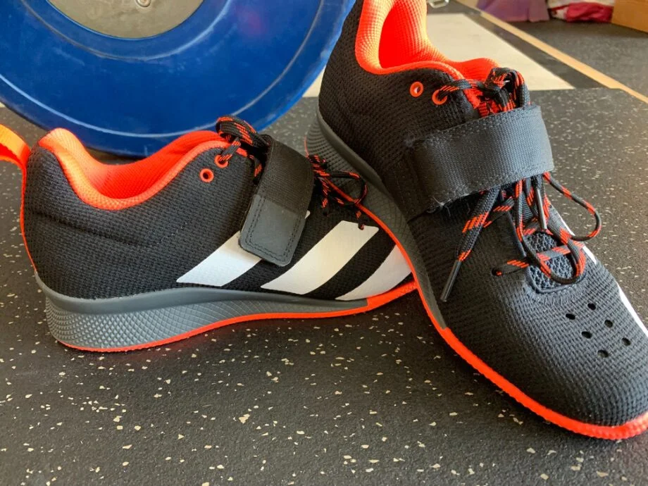 Pair of Adidas Adipower 2 weightlifting shoes near a blue bumper plate