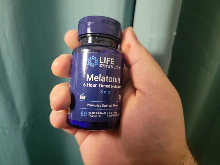 A hand holding a bottle of Life Extension Melatonin.