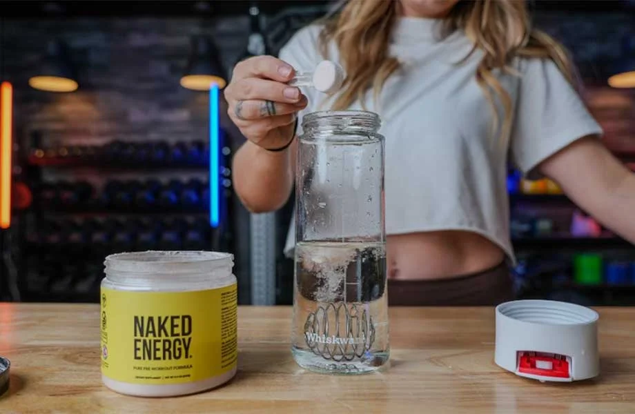 Woman dumping a scoop of Naked Pre-workout into a shaker bottle