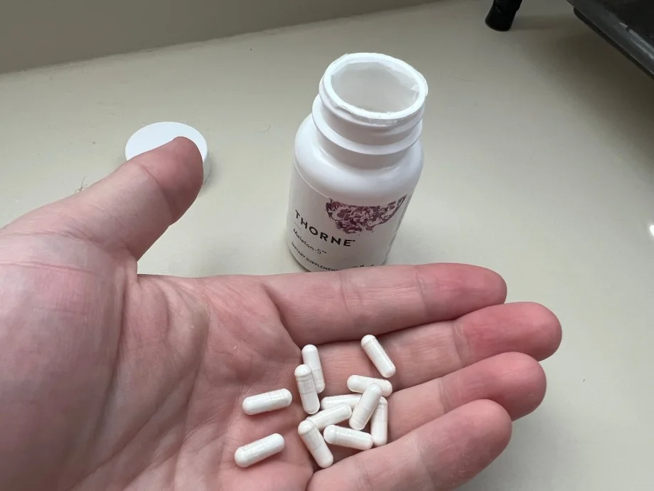 A hand holds some tiny Thorne Melatonin capsules.