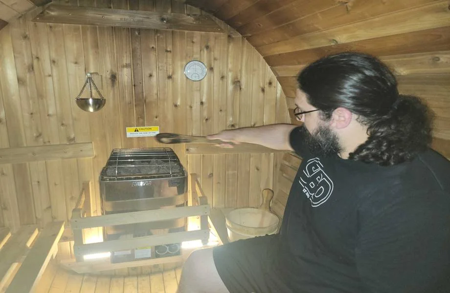 person pouring water onto heater inside almost heaven morgan barrel sauna