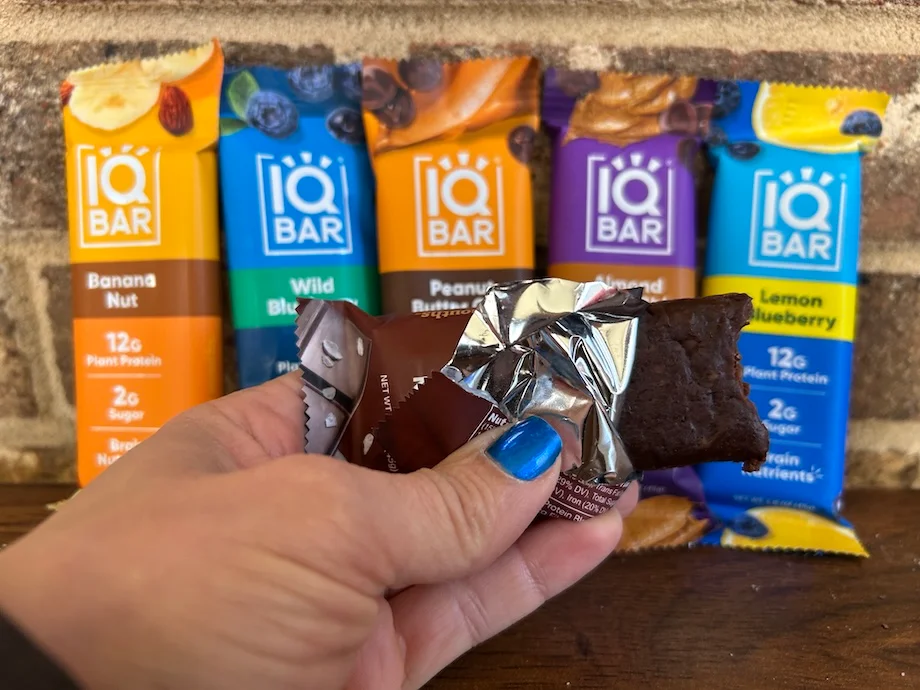 Woman holding an open IQBAR Protein Bar next to several other flavors.