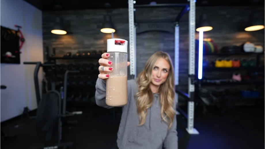 A woman holding up a shaker bottle of Transparent Labs 100% Grass-Fed Whey