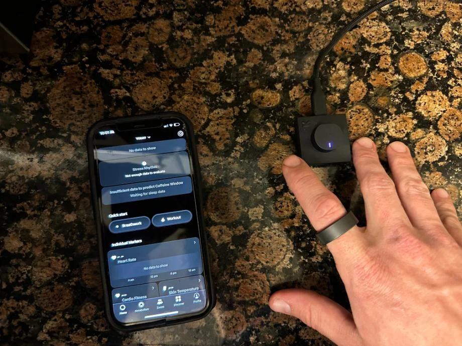 Our tester shows off Ultrahuman Ring AIR with the accompanying app and charger.