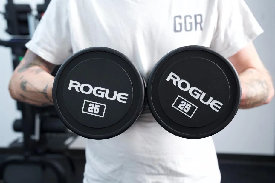 A man wearing a GGR shirt poses holding up a pair of Rogue Urethane Dumbbells