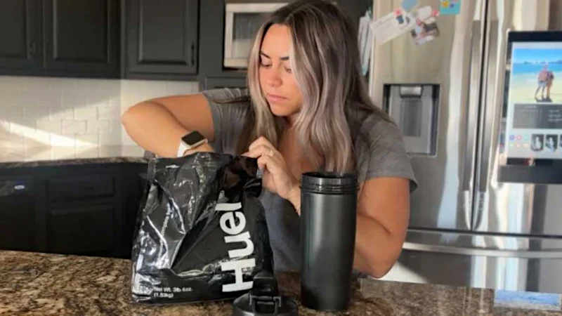 Woman scooping Huel Black out of bag into a shaker bottle