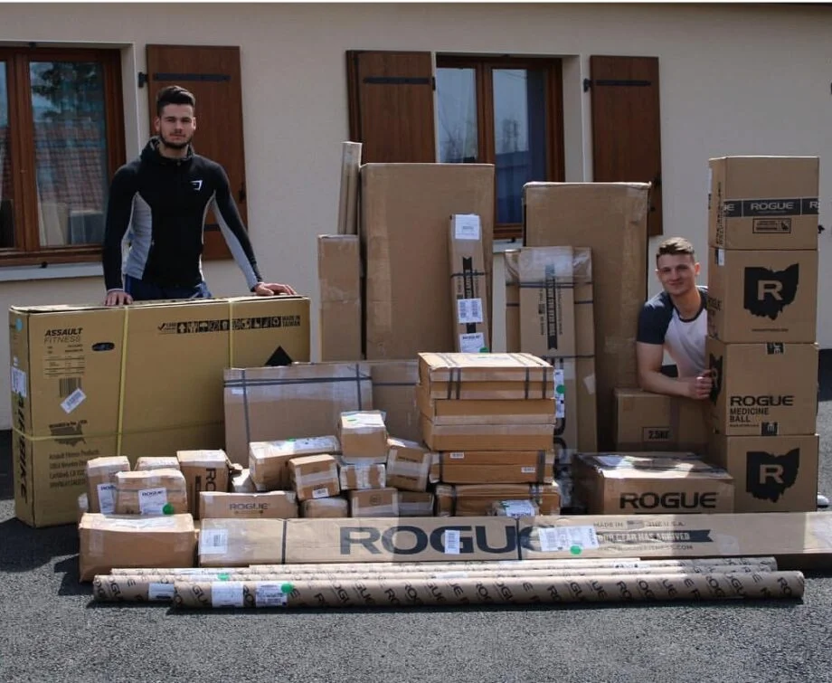 two people standing with a large shipment of Rogue fitness equipment still in shipping boxes