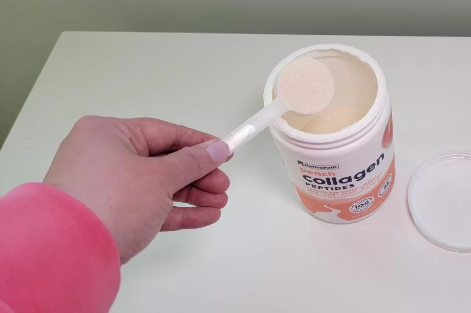 A hand takes a scoop of NativePath Collagen out of the container