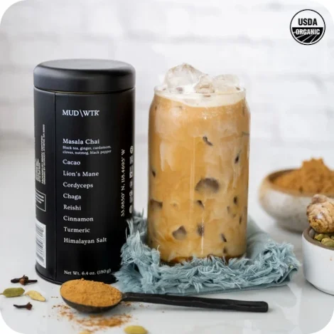 An iced glass of MUD/WTR is next to the container and a scoop.