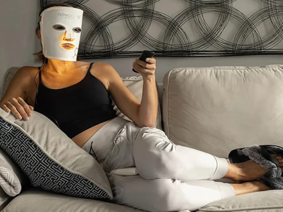 A woman using a remote control for the Novaalab Novaa Glow Therapy Mask