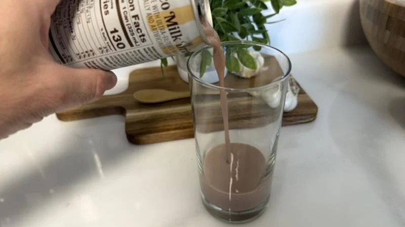 A hand pouring a can of Barebells Choco Milk Drink into a glass.