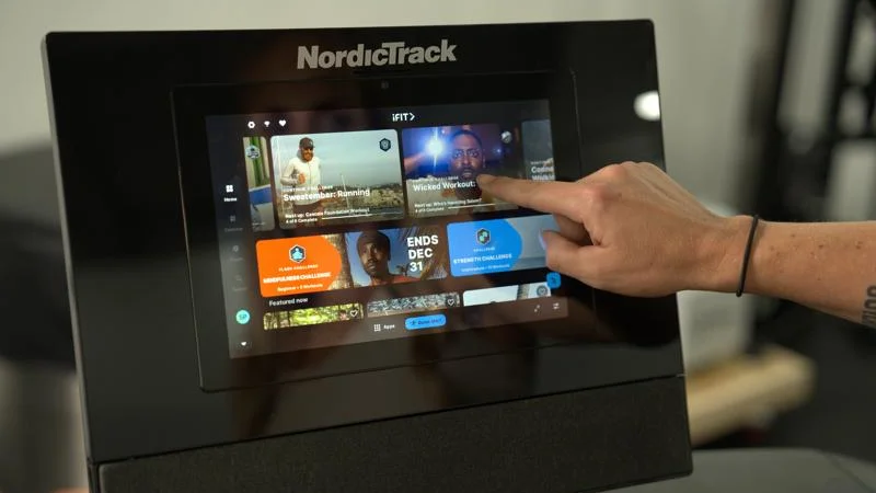 A hand reaches out to select an iFit program on the NordicTrack Commercial 1250 treadmill.