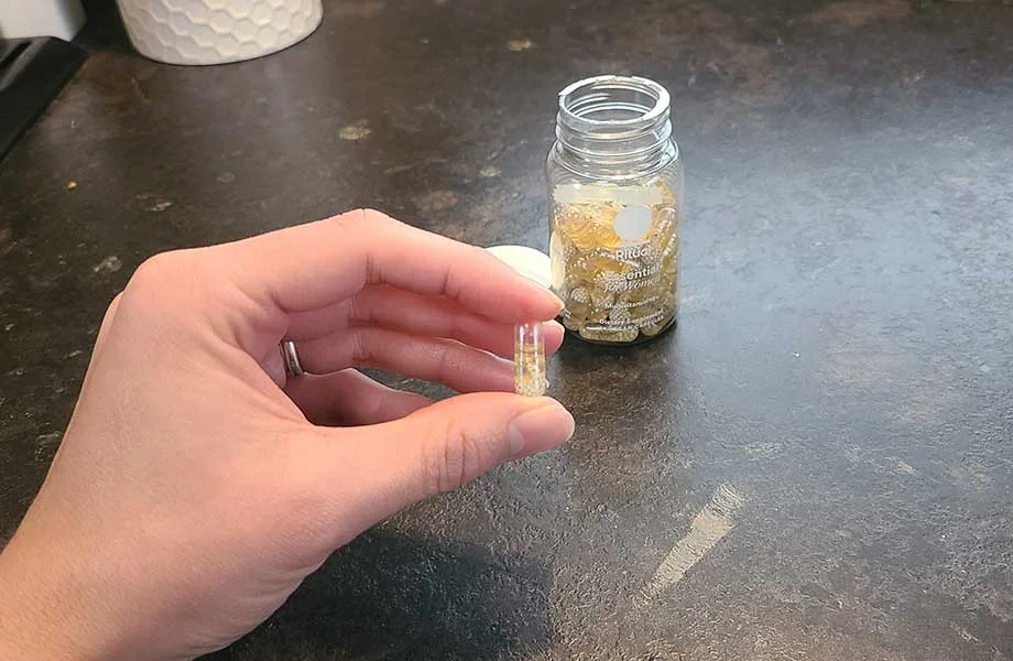 A woman holding one vegan capsule of Ritual Essential for Women 18+