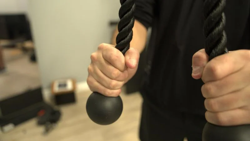 A hand holds the rope accessory for a Tonal 2 Smart Home Gym.