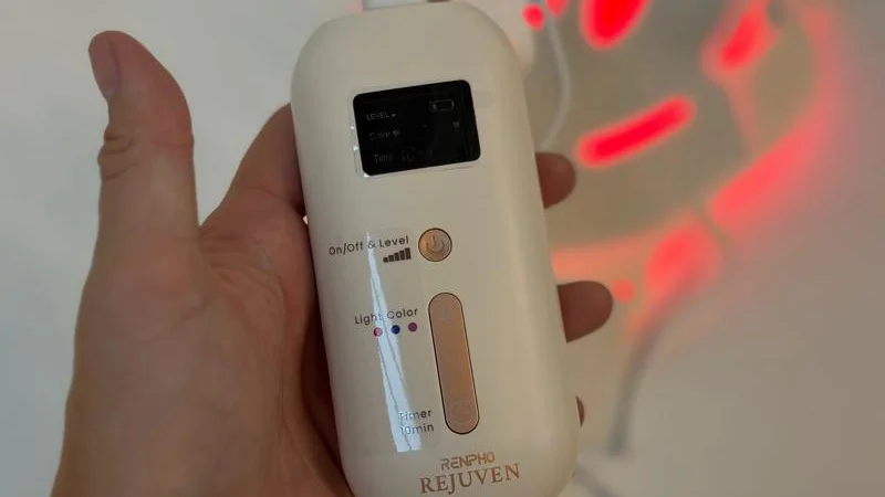 A hand holds the controls for a Renpho LED Light Therapy Mask.